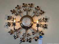 Full view of the vintage gold metal leaf design electric wall clock with two lit candle light bulbs.