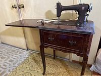 Full view of vintage dark wooden cabinet with sewing machine mounted on top, cabinet open showing workspace extension and storage drawer below.