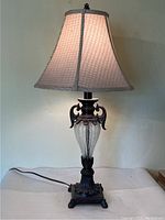 Full view of vintage style table lamp lit, showing overall form, fabric shade, glass center, and cord.