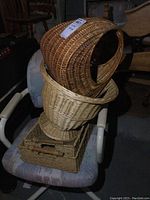 Photo of four woven baskets stacked including dark wicker urn basket with handle, light wicker basket, smaller flat woven basket.