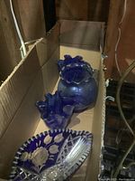 Box containing a blue glass vase with ruffled rim, two blue glass candle holders, and one blue cut crystal dish.