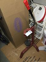 Full view of the bottle corker showing red metal frame, long handle with red grip, and black cork pressing surface.