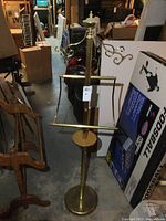 Full view of brass free standing towel rack showing round base, vertical column, scroll arms for hanging, and rectangular frame for towels.