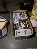 Box filled with various CDs and DVDs showing covers of different genres and titles.