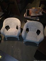 Pair of white vintage child's wicker chairs side by side on concrete floor showing seats and backs