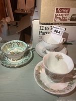 Three delicate porcelain tea cups with matching saucers arranged on a table with historic and floral designs.