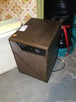 Front and side view of Mastercraft D20 dehumidifier showing control dial, vented grille, and wood-grain textured top and sides in brown.