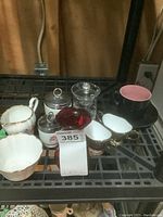 Photo showing multiple kitchenware items including egg coddlers, creamers, sugar bowls, a crystal jam jar with lid and spoon on a black rack.
