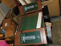 Open wooden dart board case showing green felt playing area and scoreboards on each side.