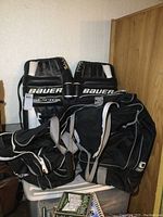 Pair of Bauer Reactor goalie pads and large hockey bag shown upright against a wall with minor wear visible on pads.