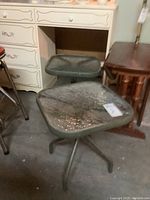 Two matching green metal outdoor side tables with textured clear glass tops shown in basement storage area.