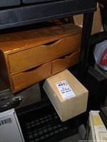 Wooden three-drawer storage box with smooth finish and integrated cutout handles shown on a shelf with other items around it.