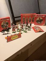 Photo showing a variety of Britains Ltd hand-painted metal toy soldiers and figurines arranged on a table with original boxes and a leaflet nearby.