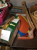 Box containing six multicolored leaf-shaped flat fan blades, partially visible in cardboard box along with another plain box