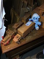 Photo of three-piece wooden toy train and two-piece transport truck on wooden surface with stuffed animal in background