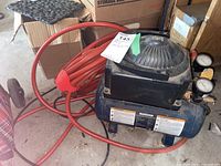 Black Mastercraft air compressor with coiled red air hose and control gauges on the front.