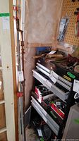 Three metal bar clamps with wooden handles leaning against a wall and next to a tool chest, showing their full height and condition.