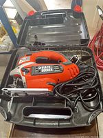 Black & Decker orange and black jigsaw with power cord inside open carrying case, showing tool details and storage compartments.