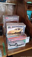 Four model car kits stacked including 1955 Chevrolet Cameo Pickup, a yellow sports car Revell Snap-Together kit, and two AMT 1996 Corvette Collector Edition kits.