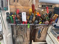 Wide view of assorted screwdrivers with red, green, black, and yellow handles, pipe wrench and small yellow level on shelf
