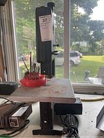 View of the band saw showing the work table, saw blade, base and red rotating tool holder with drill bits and cutting tools.
