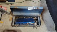 Open metal tool box showing the blue inner box on top with sockets inside and visible scattered sockets around it.