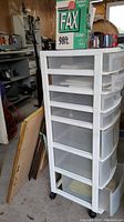 Plastic storage chest with 7 drawers shown in garage with some surrounding items and visible natural light from a window.