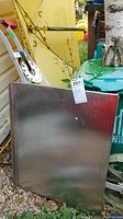 Photo of a rectangular stainless steel counter top leaning against various outdoor items. Tag #257 attached to top center.