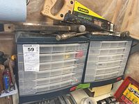 Wide view showing two plastic storage containers with drawers filled with hardware items, hand tools including hammers, and a saw resting above them.