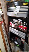 Front and side view of the Stanley metal tool box in a workshop area showing 6 drawers and under storage filled with miscellaneous items.