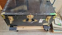 Closed black metal trunk with brass latch and lock on a wheeled dolly