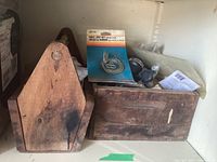 Wooden crate with darkened marks, holding plumbing accessories including sealed hardware packages and loose parts.