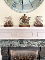 Wide shot of three bird figurines displayed on a white mantel with a large clock above