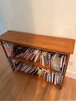 Photo of a solid wood two-shelf bookcase filled with cookbooks on both shelves.