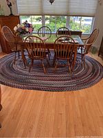 Dining room setting showing oval braided rug under wooden dining table and chairs,. Rug appears in good condition with visible color pattern and texture.