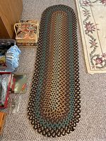 Full view of the oval braided runner rug laid out on carpeted floor with surrounding household items.