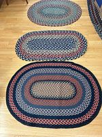 Three small oval braided rugs laid on wooden floor showing size differences and color patterns