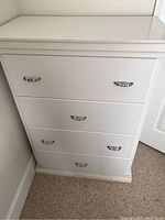 Front view of the white chest of drawers showing the 4 drawers and silver-tone handles.