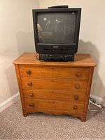 Front view of wooden chest of drawers with 4 drawers and a vintage Magnavox TV on top.