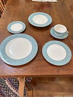 Dishes including dinner plates, salad plates, bread and butter plates, and cups with saucers showing the blue and white floral border design.