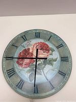 Front view of large round wall clock showing Roman numerals and floral design with roses