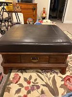 Front view showing wooden base with drawer and dark leather cushioned top.