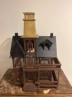 Front view of the decorative wood bird cage shaped like a Victorian house, showing detailed window frames, front staircase, and chimney stack.