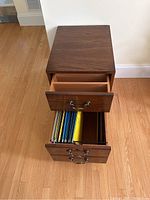 Top view of wood file cabinet with top drawer open, showing a plain wooden interior. Bottom drawer open showing hanging file folders inside.
