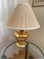 Side view of gold color metal lamp with cream pleated shade on glass side table.