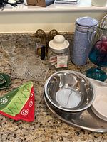 Overview of various dishware on granite countertop including glassware, stainless steel bowls and tray, and ceramic plates.