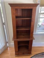 Front image of a narrow wooden hutch with multiple shelves, one drawer at the bottom and open compartments. The wood finish is medium brown with visible natural grain and panel details.