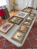 Overall view of nine framed paintings laid out on a table, showing various sizes and frame styles.