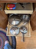 Drawer with three stainless steel pots/pans with lids and one smaller stainless steel pan without lid, all stacked or laid out.