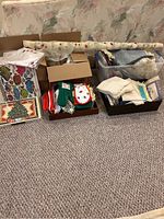 Overview of assorted linens including fabric roll, potholders, placemats, and folded cloths spread on carpet in front of a floral couch